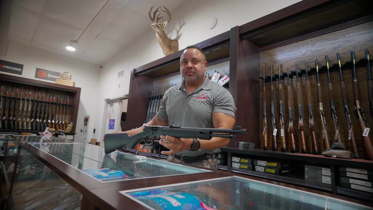 A member of the Mumme's gun room staff presenting a lever-action shotgun across the counter